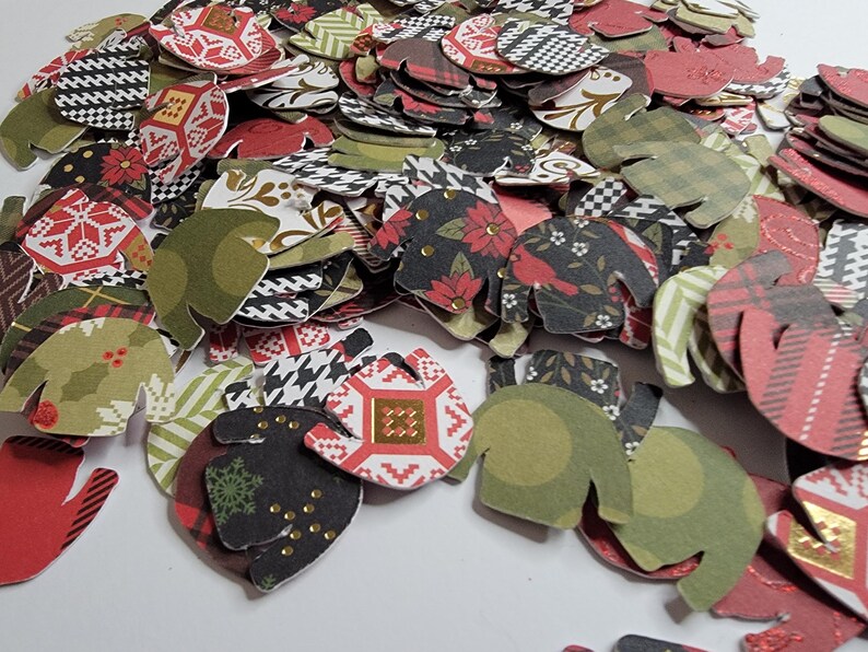 May include: A large pile of colorful paper cutouts shaped like sweaters. The cutouts feature various holiday patterns, including plaid, snowflakes, and geometric designs.