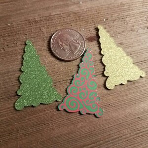 Puede incluir: Tres recortes de &aacute;rboles de Navidad, uno verde, uno dorado y uno con un patr&oacute;n de espiral rojo y verde.