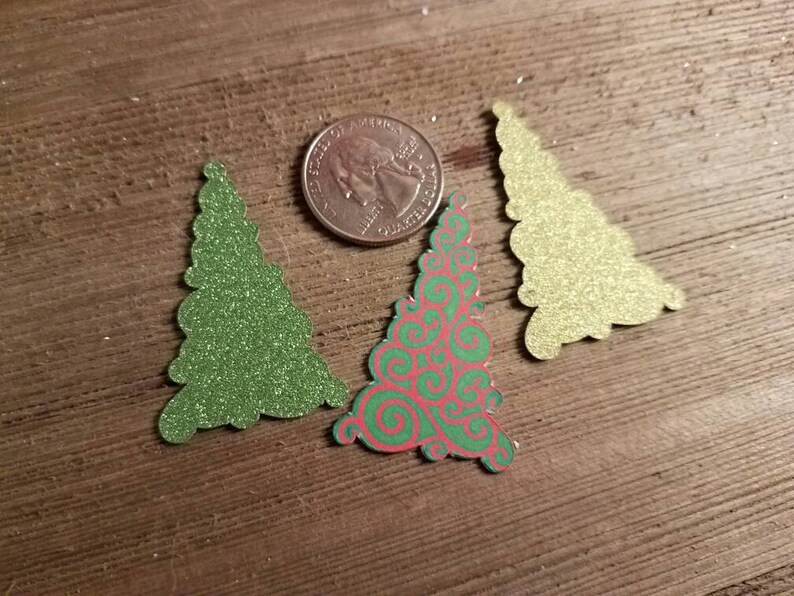 Puede incluir: Tres recortes de &aacute;rboles de Navidad, uno verde, uno dorado y uno con un patr&oacute;n de espiral rojo y verde.