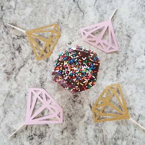 Pu&ograve; includere: Quattro topper per torta a forma di diamante, due dorati e due rosa, con un ciambellone al cioccolato ricoperto di codette colorate al centro.