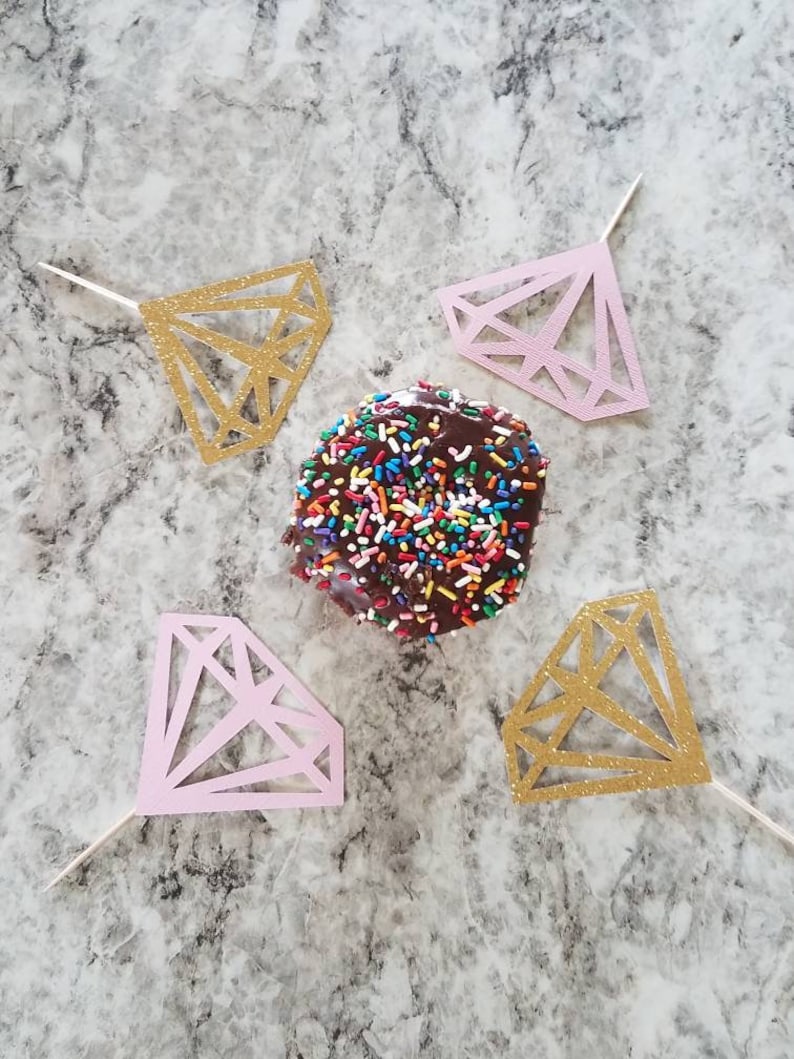 Pu&ograve; includere: Quattro topper per torta a forma di diamante, due dorati e due rosa, con un ciambellone al cioccolato ricoperto di codette colorate al centro.