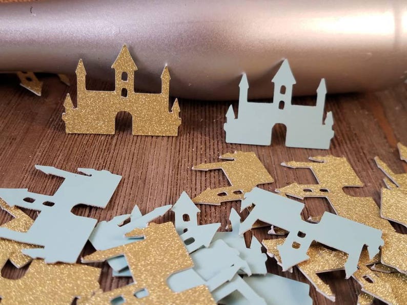 May include: A pile of gold and light blue glitter castle confetti. The confetti is in the shape of a castle with towers and a pointed roof.