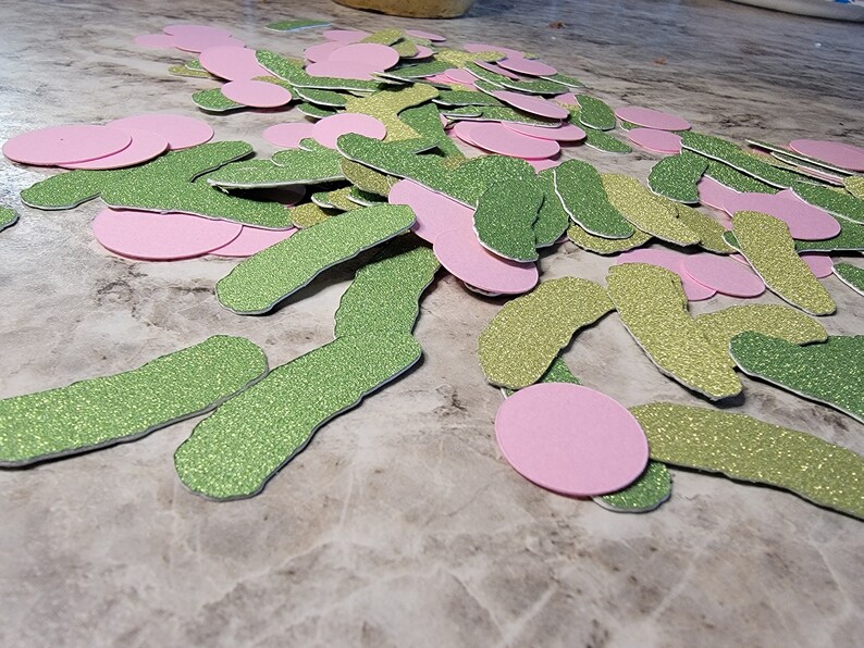 May include: A pile of green and pink glitter paper cutouts in the shape of a worm and circles.