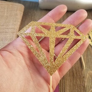 Pu&ograve; includere: Topper per cupcake a forma di diamante dorato con glitter e un bastoncino di legno.