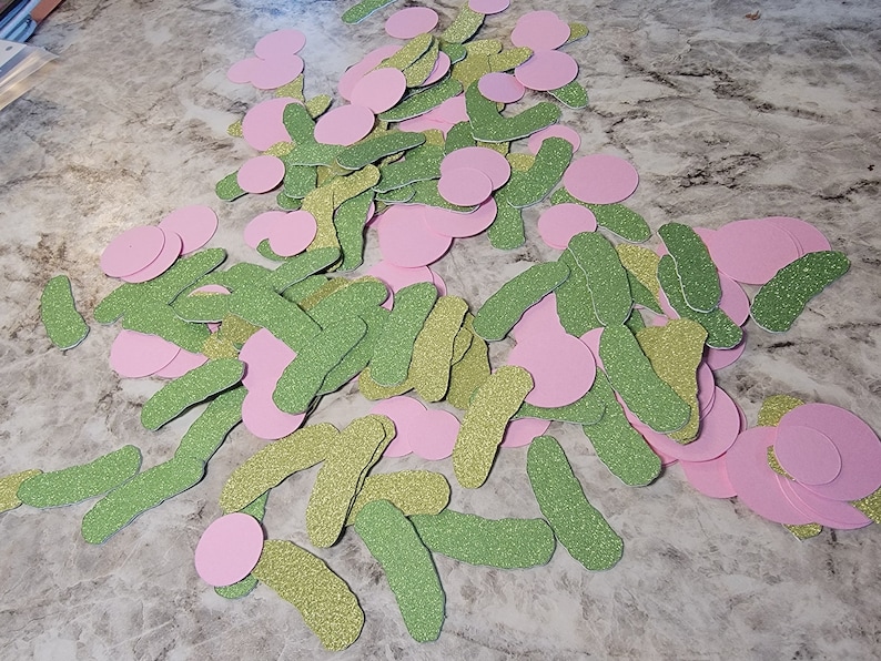 May include: A pile of green and pink glitter paper cutouts. The cutouts are shaped like pickles and circles.