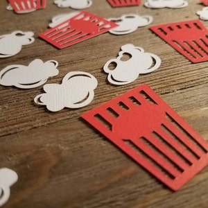 May include: Red and white paper cutouts of popcorn and popcorn boxes on a wooden surface.