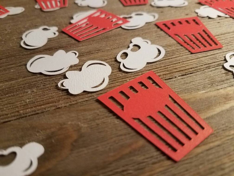 May include: Red and white paper cutouts of popcorn and popcorn boxes on a wooden surface.