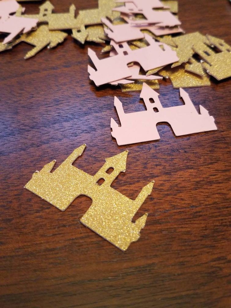 May include: A pile of pink and gold glitter castle confetti. The castles are cut out of paper and have a sparkly finish.