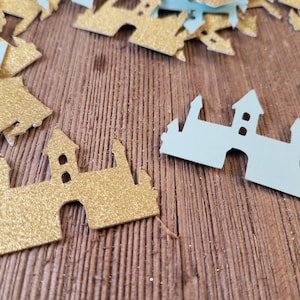 May include: A pile of gold and light blue glitter castle confetti. The confetti is scattered on a wooden surface.