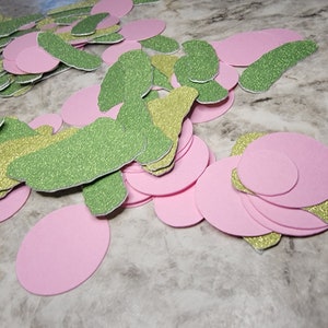 May include: A pile of green and gold glitter paper cutouts in the shape of a butterfly, and pink paper circles.