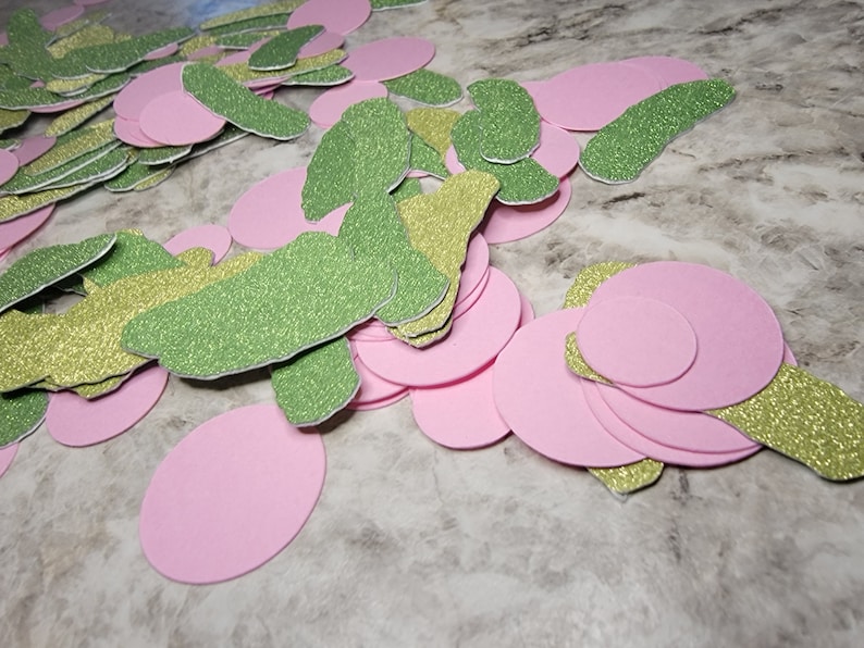 May include: A pile of green and gold glitter paper cutouts in the shape of a butterfly, and pink paper circles.