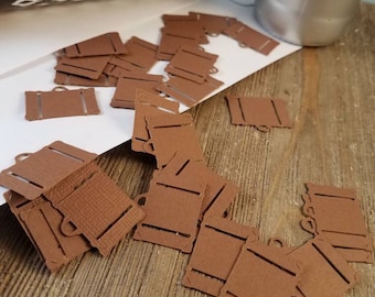 Könnte beinhalten: Ein Stapel brauner Papieretiketten mit einem ausgeschnittenen Design. Die Etiketten sind auf einer Holzoberfläche verstreut.