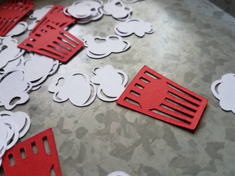 May include: Red and white paper cutouts of popcorn and popcorn boxes. The cutouts are scattered on a gray surface.