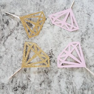 Pu&ograve; includere: Quattro topper per torta a forma di diamante, due con glitter dorati e due rosa. I topper sono fatti di carta e hanno un bastoncino sul retro per inserirli in una torta.