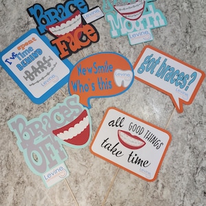 May include: A set of 7 colorful photo booth props with a braces theme. The props feature phrases like "Brace Face", "Metal Mouth", "New Smile Who's This", "Got Braces?", "I've Spent Time Behind Bars", "Braces Off", and "All Good Things Take Time".
