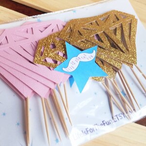Pu&ograve; includere: Un pacchetto di topper per cupcake a forma di diamante con glitter rosa e oro, con un topper a forma di stella blu che dice "Life is for the fun" con un baffo.