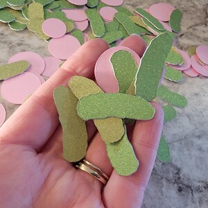 May include: A hand holding a pile of green and pink glitter paper cutouts. The cutouts are shaped like pickles and circles.
