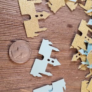 May include: A pile of gold and light blue glitter castle confetti. The confetti is in the shape of a castle with towers and windows.
