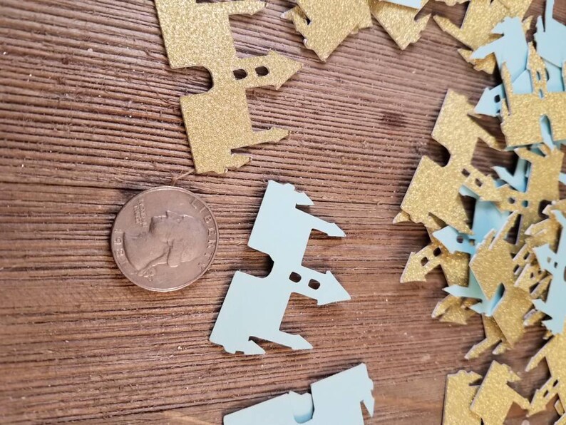 May include: A pile of gold and light blue glitter castle confetti. The confetti is in the shape of a castle with towers and windows.
