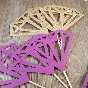 Pu&ograve; includere: Topper per torta a forma di diamante, di colore viola e oro, con bastoncini di legno. I diamanti sono ritagliati e hanno una finitura glitterata.
