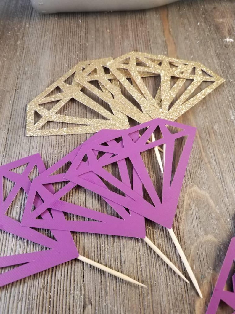 Pu&ograve; includere: Topper per torta a forma di diamante, di colore viola e oro, con bastoncini di legno. I diamanti sono ritagliati e hanno una finitura glitterata.