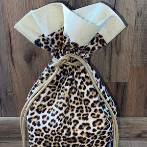 May include: A leopard print drawstring bag with a white, glittery top. The bag has a gold drawstring.