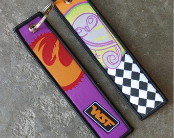May include: Two embroidered keyrings with metal hoops. One is purple with an orange flame design and the letters "WSF". The other is orange, green, and white with a cartoon design and a black and white chequered pattern.