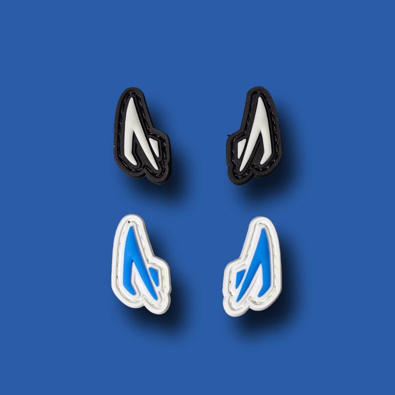 Pu&ograve; includere: Quattro ciondoli per scarpe, due neri e due bianchi, con un design blu e bianco. I ciondoli hanno la forma di una lettera A stilizzata.