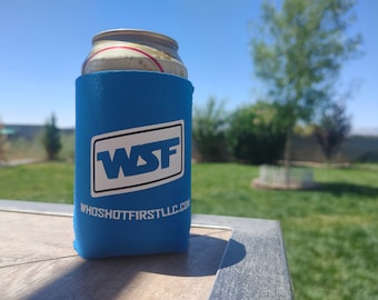 May include: A blue can cooler with the text "WSF" and "WHOSHOTFIRSTLLC.COM" printed on it. The cooler is holding a can of beer.