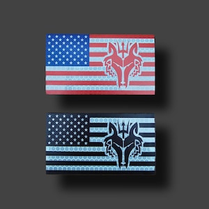 May include: Two rectangular patches featuring an American flag design with a wolf head emblem. One patch has a red, white, and blue color scheme, while the other is black, white, and gray. The patches have a reflective surface.