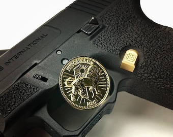 May include: A black handgun with a gold-colored coin on the side. The coin has a lion design and the text "PASCAL SABSU" around the edge.