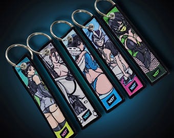 May include: Five keychains featuring anime-style illustrations of women. Each keychain has a different design, with a metal ring and a rectangular fabric tag. The tags feature a variety of colours, including green, blue, pink, and black, with the text "WSF" on each.