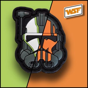 May include: A black patch featuring a split design of a helmet, with one half white and green, the other orange. The patch has a detailed, geometric design and the letters "WSF" in a white box.