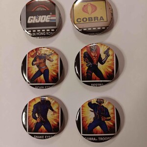 May include: Six round button pins featuring characters from the G.I. Joe cartoon. The pins feature Cobra, Destro, Scarlett, Snake Eyes, and Cobra Trooper.