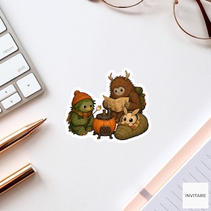 May include: A die-cut sticker featuring a green creature in an orange beanie and scarf roasting a marshmallow, a brown furry creature with antlers reading a map, and a small moth-like creature in a sleeping bag near a pumpkin-shaped stove.