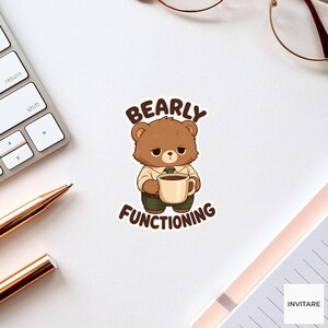 May include: A die-cut sticker featuring a brown cartoon bear with a tired expression, wearing a tan shirt and dark green trousers, holding a beige coffee mug. The text BEARLY FUNCTIONING is printed in dark brown letters above and below the bear.