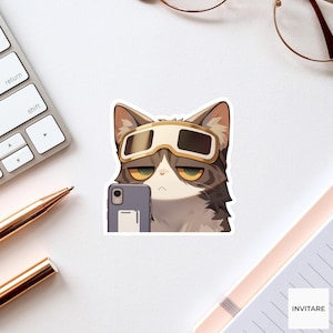 May include: A die-cut sticker featuring a brown and white cat with yellow eyes wearing gold-rimmed goggles. The cat is holding a gray smartphone in front of its face, appearing to take a selfie. The illustration has a flat, clean aesthetic.