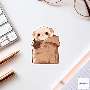 Könnte beinhalten: Ein gestanzter Aufkleber mit einer Cartoon-Illustration eines hellbraunen Frettchens mit dunkelbraunen Pfoten, das aus der Vordertasche eines beigen Kapuzenpullovers schaut. Das Frettchen hat große dunkle Augen und ein kleines Lächeln.