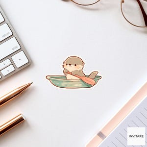 May include: A die-cut sticker featuring a light brown cartoon otter sitting in a small, teal-colored rowboat. The otter is holding a wooden-colored oar, paddling through the water. The illustration has a clean white border around the edges.