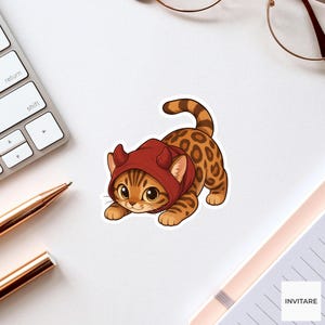 May include: A sticker featuring a cartoon Bengal cat with brown spots and a long tail. The cat is wearing a dark red hood with two small devil horns on top. The cat has large, expressive eyes and is depicted in a playful, crouching position.