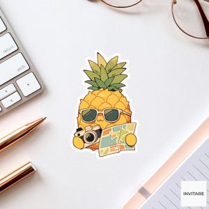 May include: A die-cut sticker featuring a yellow pineapple character wearing light-coloured sunglasses. The pineapple holds a black camera in one hand and an open, multi-coloured map in the other, with green leaves on top and a white border outline.