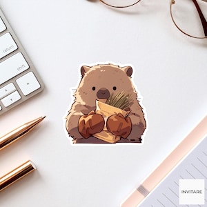Peut inclure: Un autocollant découpé représentant un wombat de style dessin animé brun clair avec des pattes brun foncé. Le wombat tient un sac en papier beige rempli d'herbe verte. L'illustration présente une bordure blanche et une finition mate.