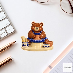 May include: A brown bear figurine wearing blue overalls, sitting at a pottery wheel and shaping a clay pot. The scene includes a small blue and white container with tools, a small bowl of water, and an empty clay pot on a round base.