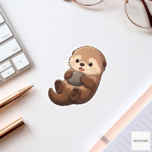 May include: A die-cut sticker featuring a cartoon brown sea otter with a light tan face and belly, holding a smooth gray rock against its chest. The otter has a small pink tongue visible, dark eyes, and a white outline on a white background.