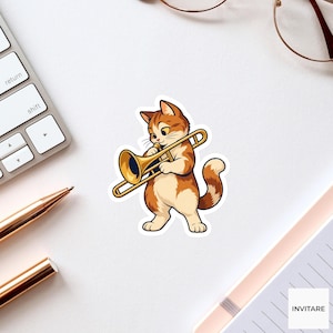 Puede incluir: Una pegatina troquelada que muestra a un gato atigrado naranja y blanco tocando un trombón dorado. El gato tiene ojos grandes y está de pie. La pegatina tiene un borde blanco y está colocada sobre una superficie blanca junto a un teclado.