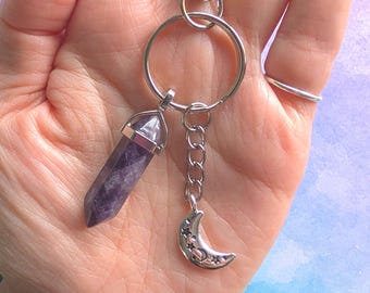 May include: A silver-toned keychain featuring a polished, hexagonal purple amethyst crystal point encased in a metal cap, paired with a small silver crescent moon charm decorated with cut-out star shapes, all attached to a circular ring and lobster clasp.