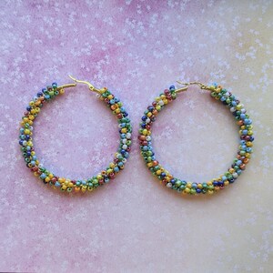 May include: A pair of large hoop earrings made with colorful seed beads. The beads are arranged in a spiral pattern and are a mix of green, blue, yellow, red, and white.