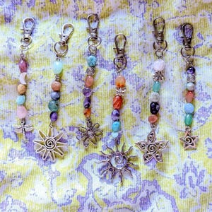 May include: Six silver-toned metal keychains featuring assorted colorful gemstone beads and charms. The charms include a dragonfly, a sun, a flower, and a star. Each keychain is attached to a lobster clasp, showcasing various natural stone shapes.