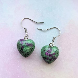 May include: A pair of heart-shaped earrings with green and pink gemstone accents. The earrings are made of stainless steel and have a simple hook fastening.