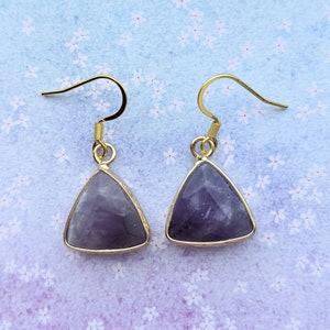 May include: A pair of gold triangle earrings with amethyst stones. The earrings have a simple design and are perfect for everyday wear.